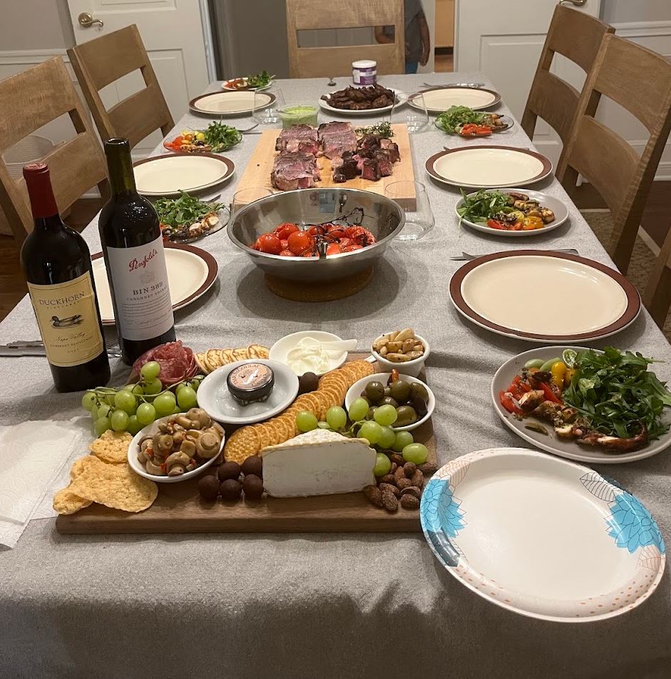 Spread of food including a charcuterie board, steak, tomatoes, and salad